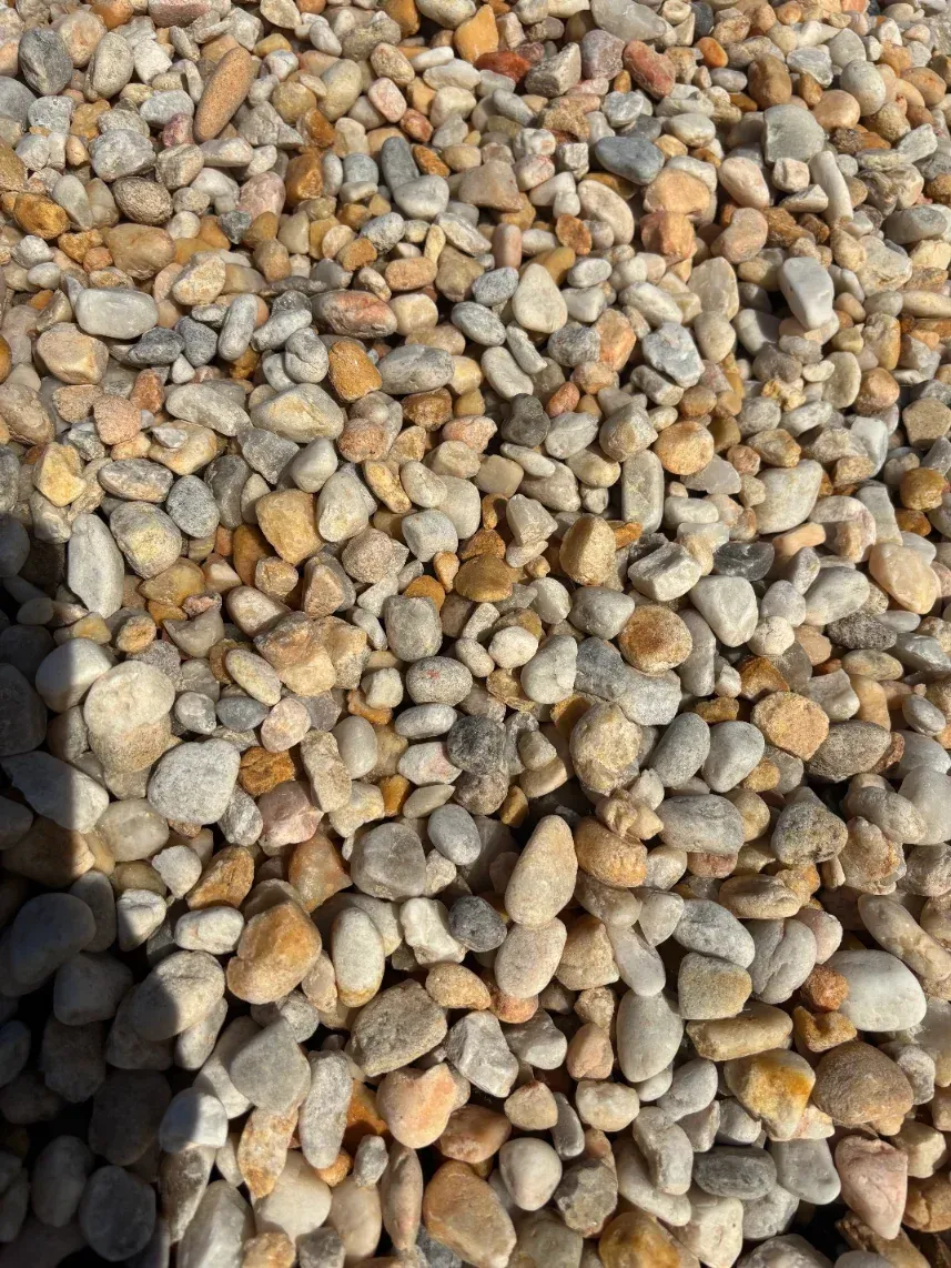 Close-up of small tan and gray pebbles, with a dark shadow along the left edge.