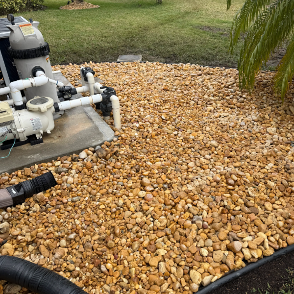Pool equipment beside a bed of tan rocks and grass in a landscaped yard.