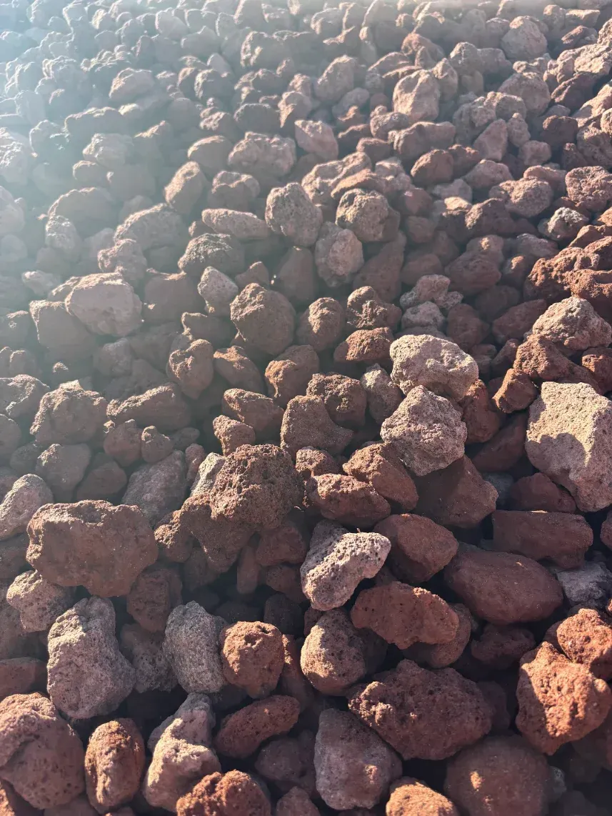 Pile of rough, reddish-brown rocks or rubble filling the frame, lit by sunlight from the upper left.