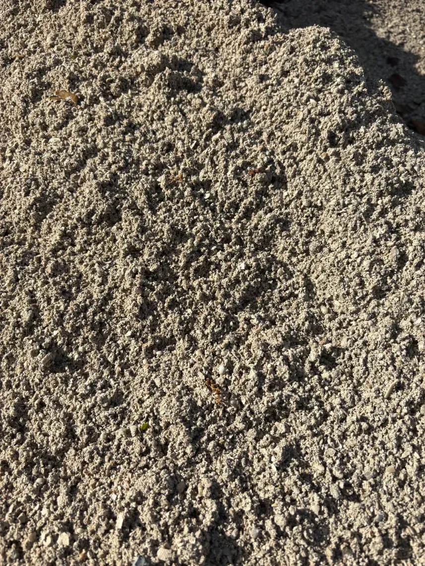 Close-up of rough beige gravel or sand with sunlight casting shadows across the textured surface
