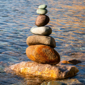 Stack of balanced stones on a wet beach, with rippling water in the background.