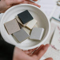 Hands holding a bowl of small square tile samples in beige, gray, white, and dark green