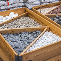 Wooden bins filled with assorted decorative stones and pebbles in white, gray, beige, and brown.