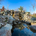 Rocky pond with still water reflecting a blue sky and sunlight on the stones.
