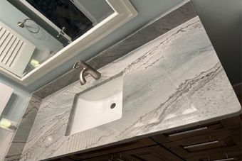 Oak cabinetry with a granite countertop, open shelves, and sage green beadboard backsplash in a kitchen.