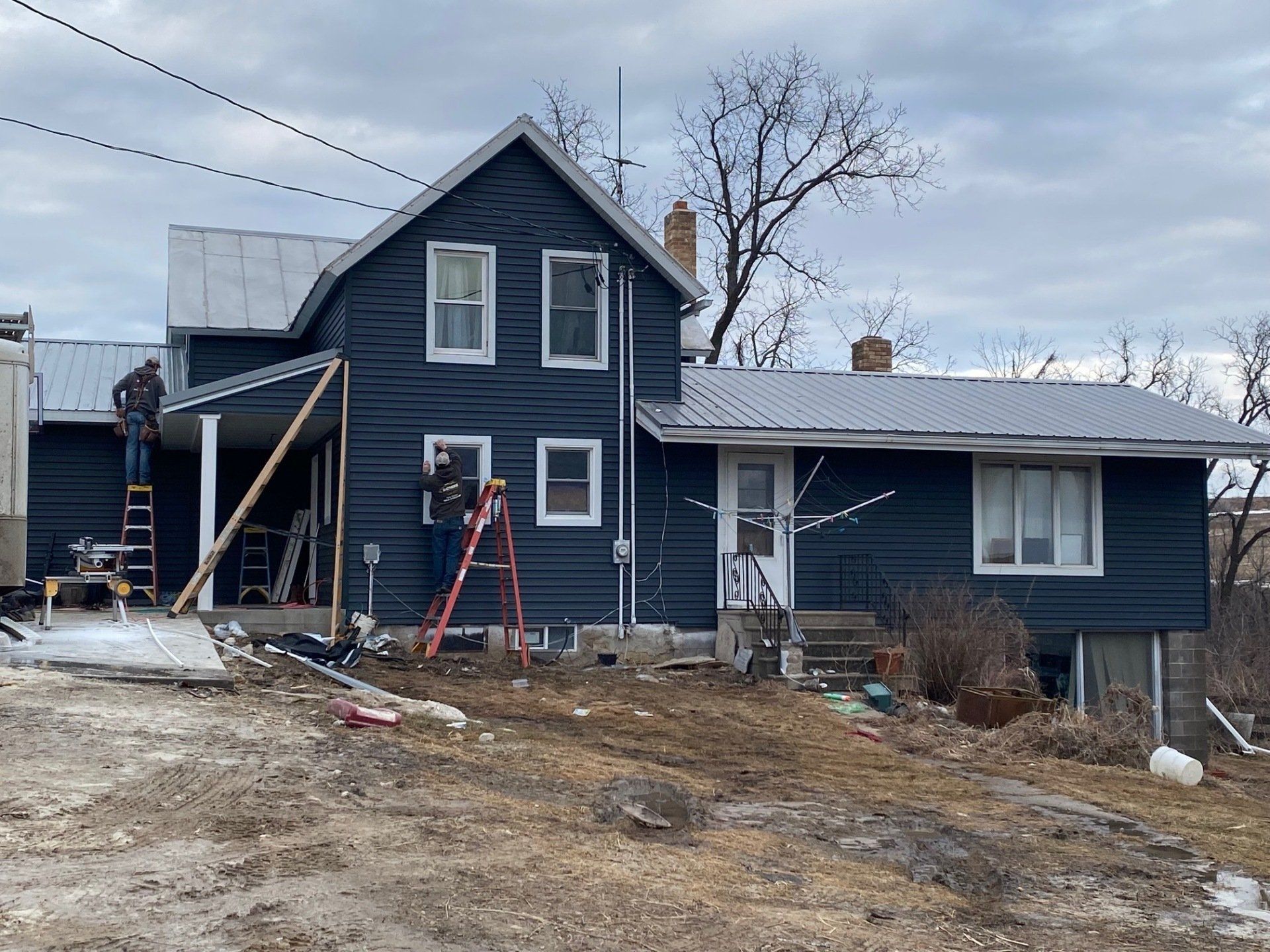 Two-story blue house under construction; workers on ladders. Overcast day.