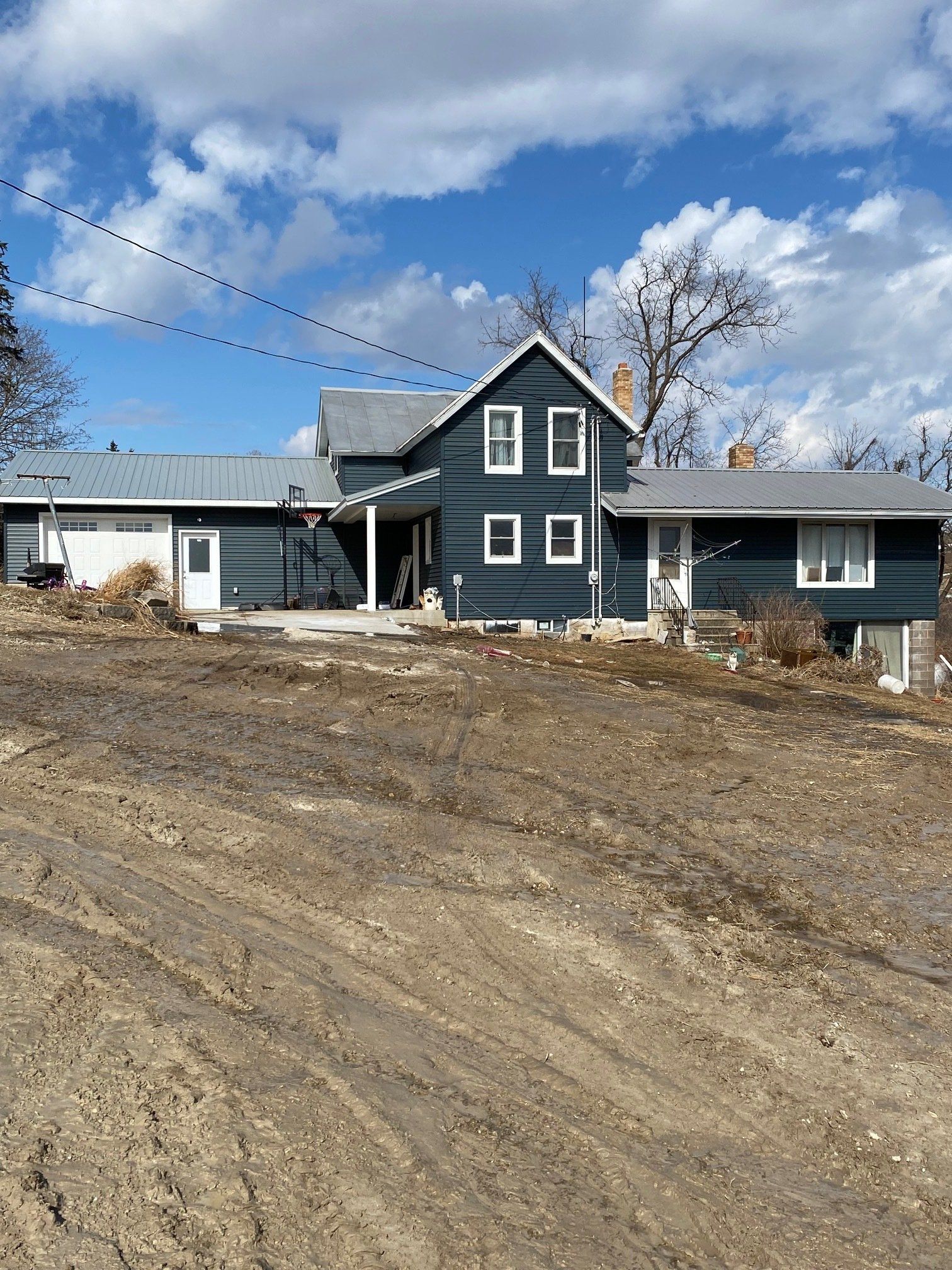Dark blue house with white trim, set on a graded dirt lot under a cloudy sky.