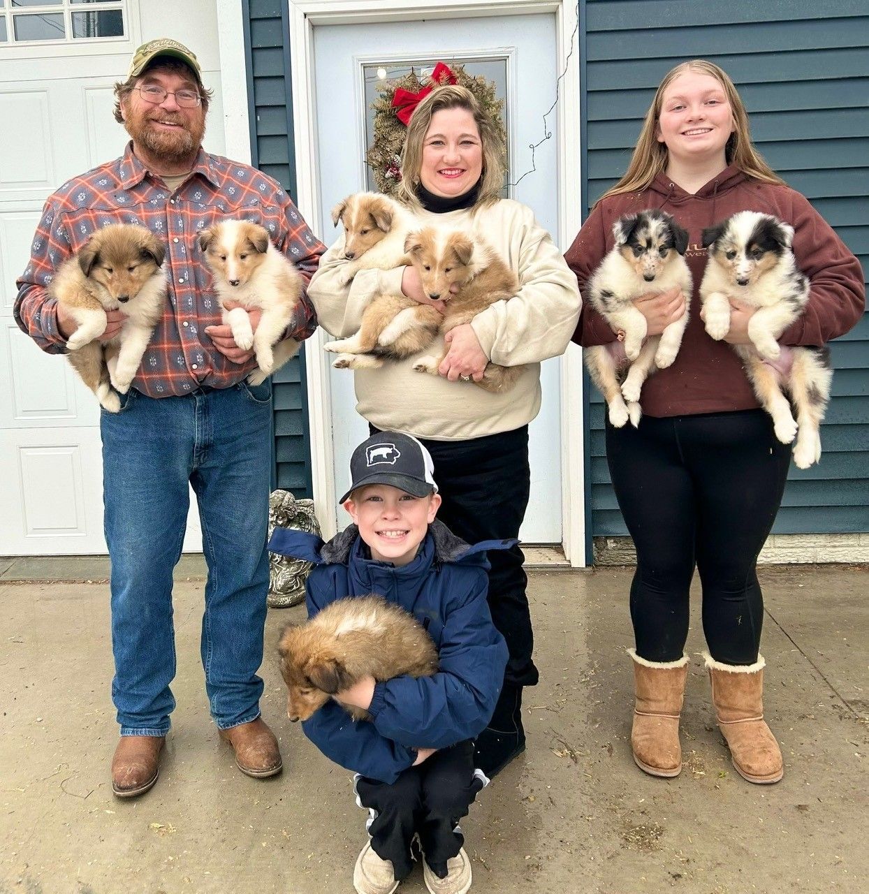 Family holding puppies in front of a blue building with a wreath.