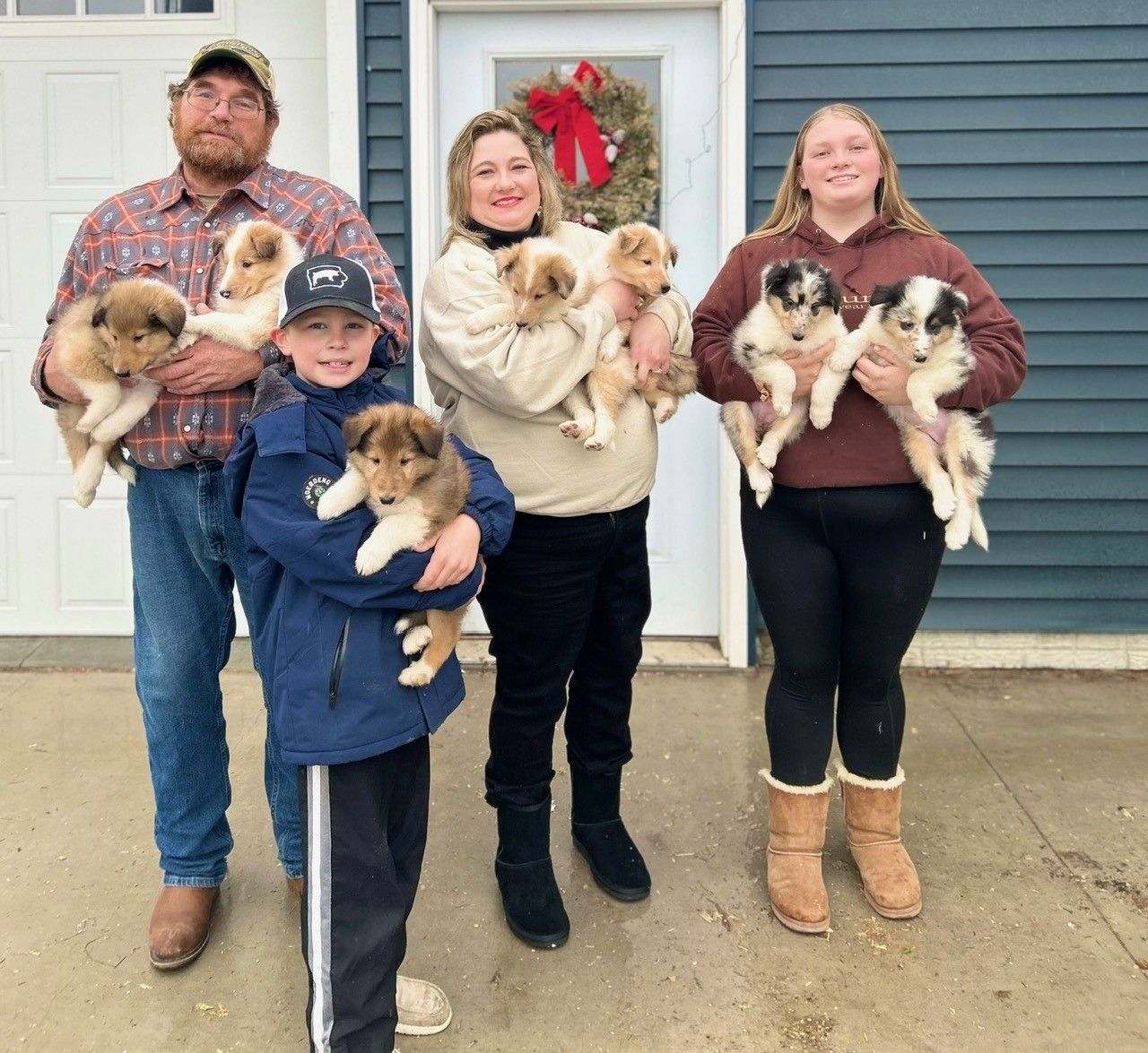 Family holding puppies in front of a house with a holiday wreath.