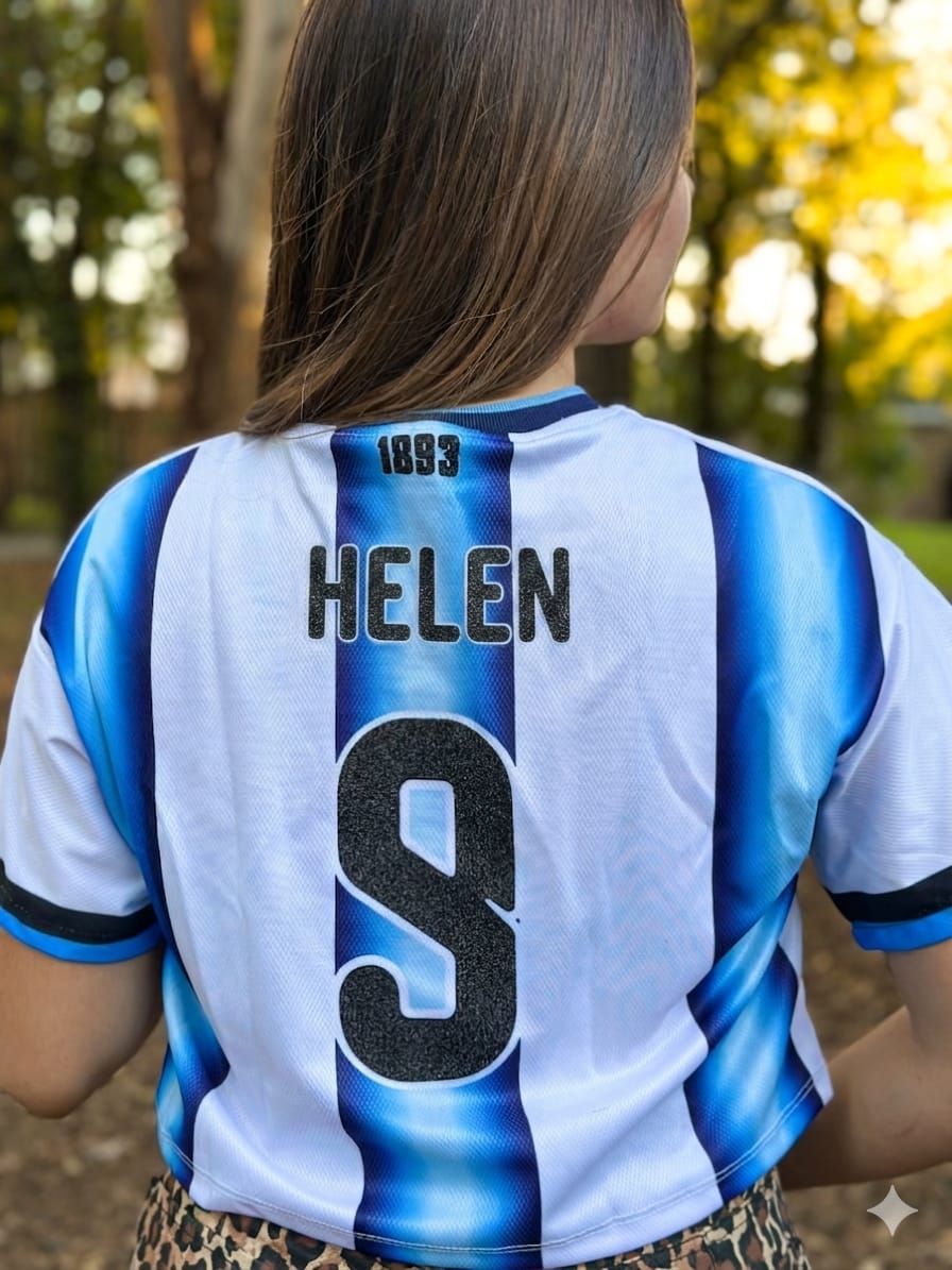 Vista trasera de una persona con una camiseta azul y blanca con la palabra “HELEN” y el número 9 al aire libre.