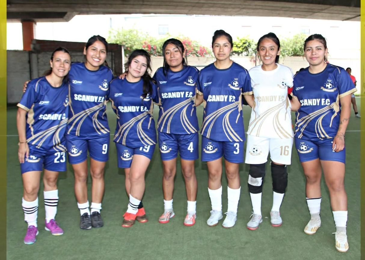 Siete mujeres con uniformes de fútbol azules posando juntas en un campo, una de ellas con equipación blanca de portera.