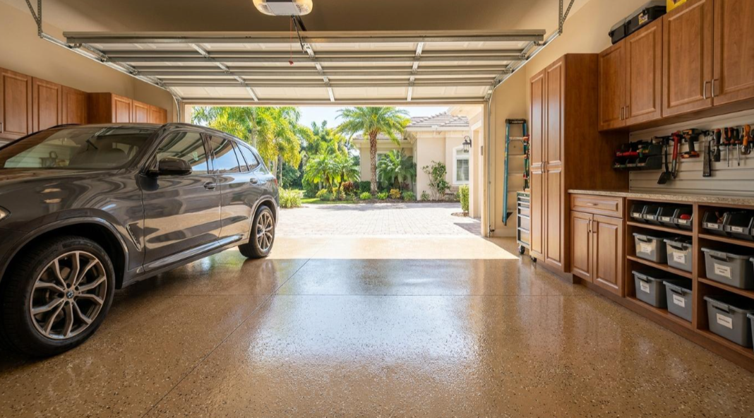 Open garage with parked SUV and built-in cabinets, looking out to a sunny driveway and garden.