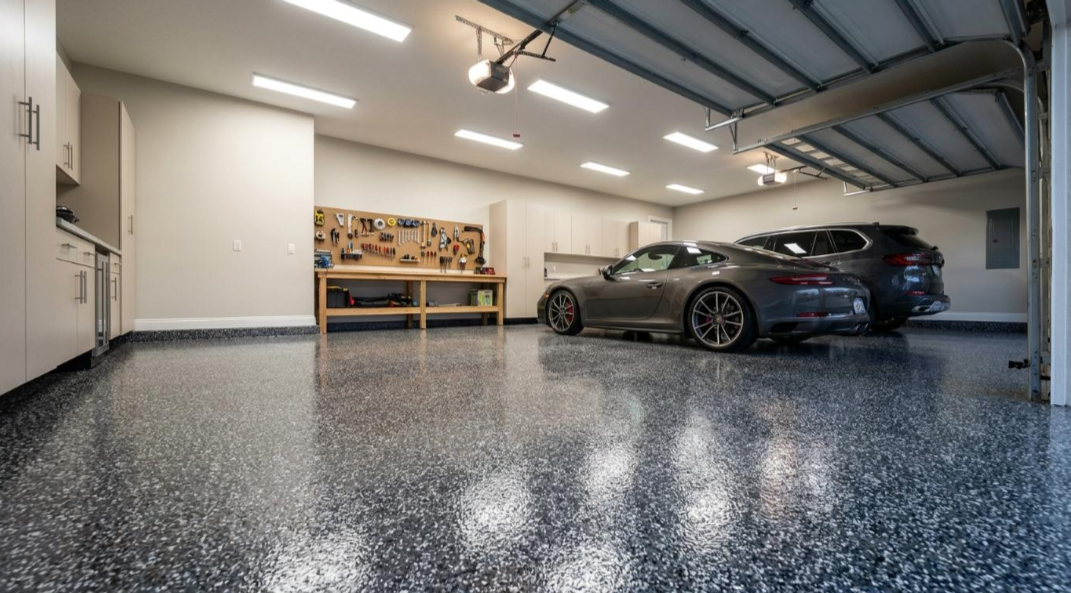 Modern garage with a gray sports car, black SUV, and workbench on a speckled epoxy floor