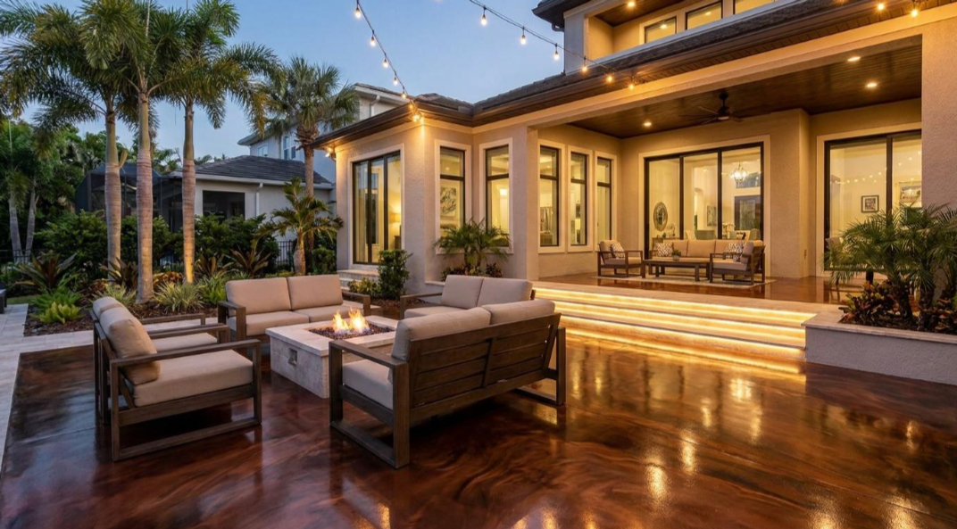 Luxury patio at dusk with wicker seating, warm lighting, and a reflective wooden deck beside a modern home