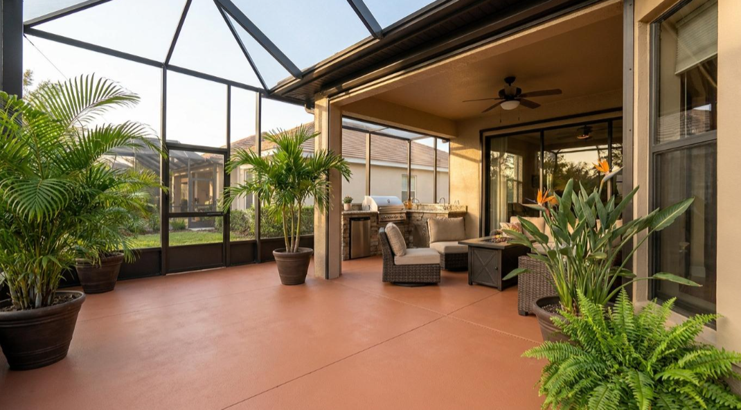 Indoor patio with terracotta tile, potted palms, wicker chairs, and screened glass walls under a covered ceiling