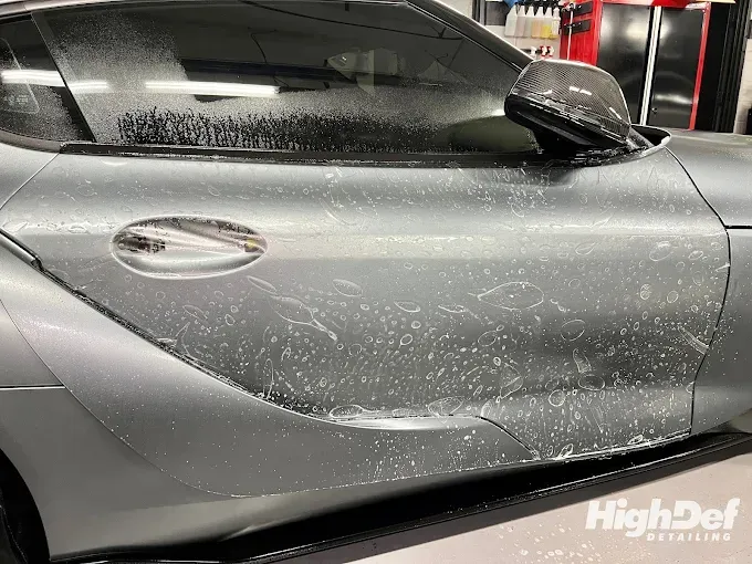 Close-up of a car door during paint protection film installation, showing the protective film being 