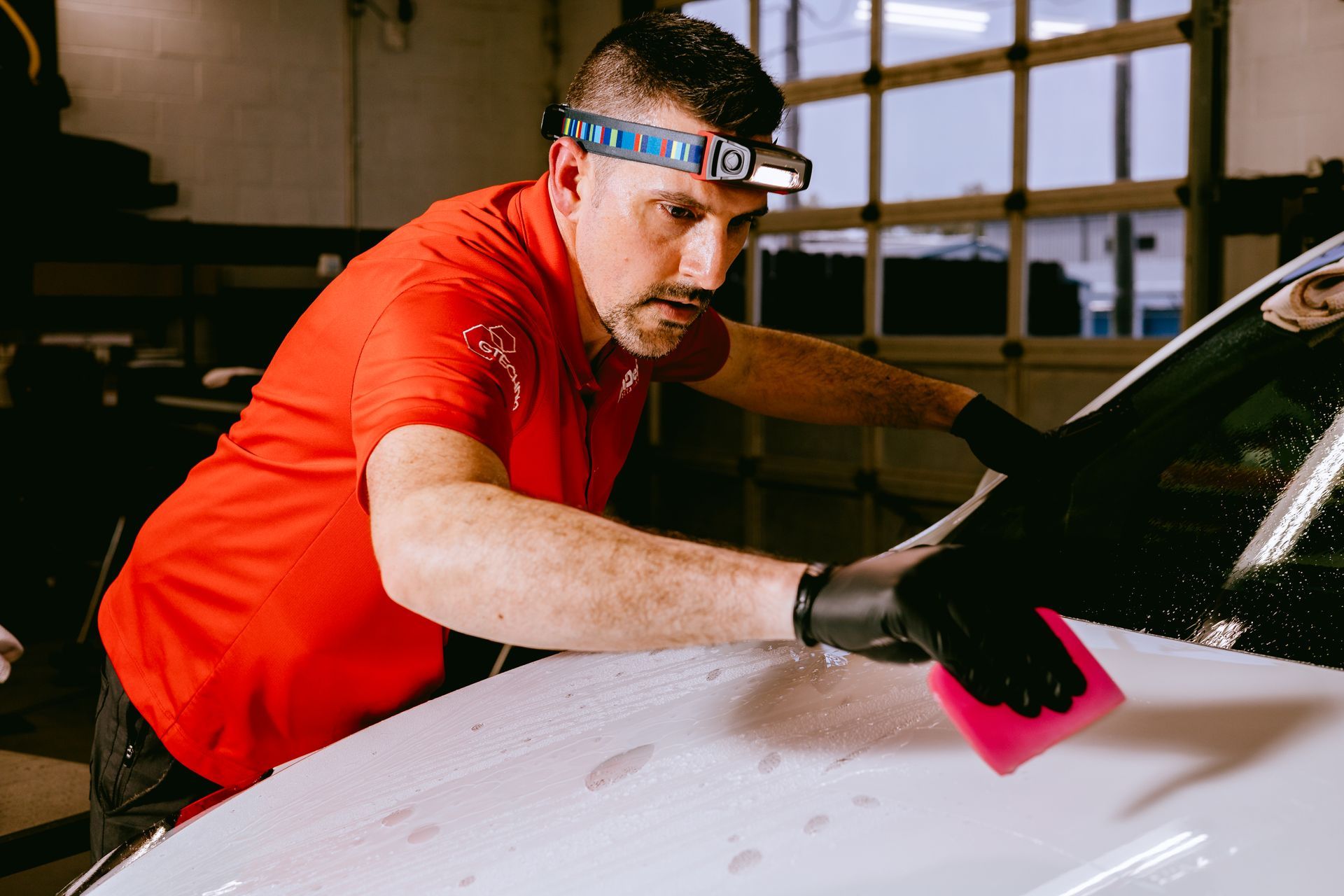 a man in a red shirt is cleaning the windshield of a white car .