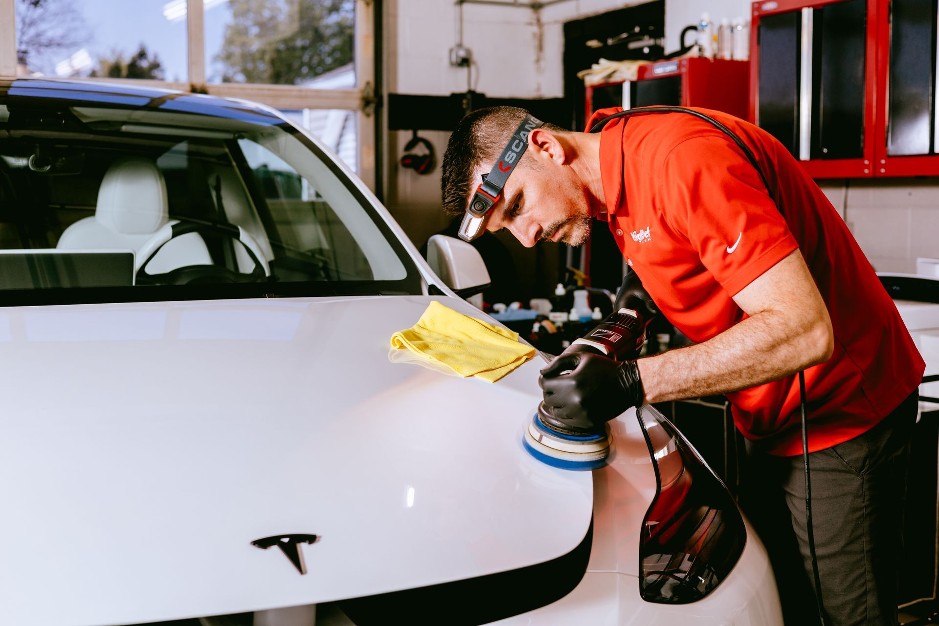 Detailing a white Tesla with a buffer in a workshop