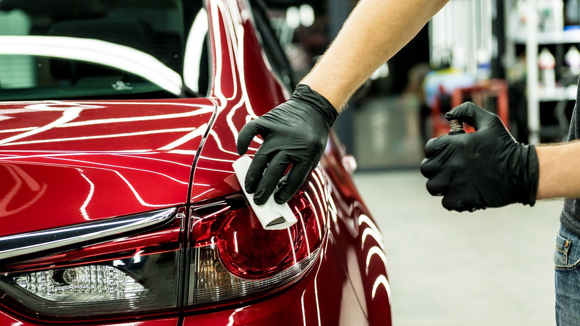 A person wearing black gloves is polishing a red car.