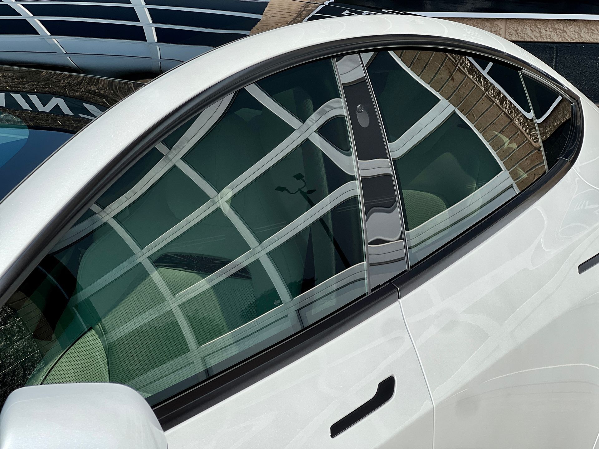 White car door with a partially open window, showing a building reflected in the glass.