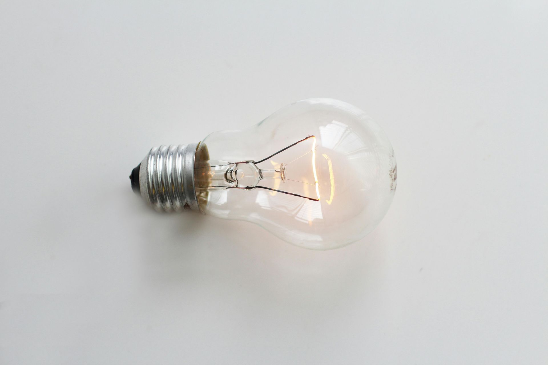 A lit incandescent lightbulb on a white surface.