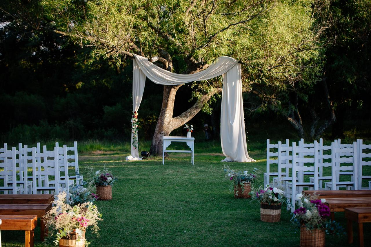 Una boda al aire libre ambientada sobre césped con sillas blancas, arreglos florales