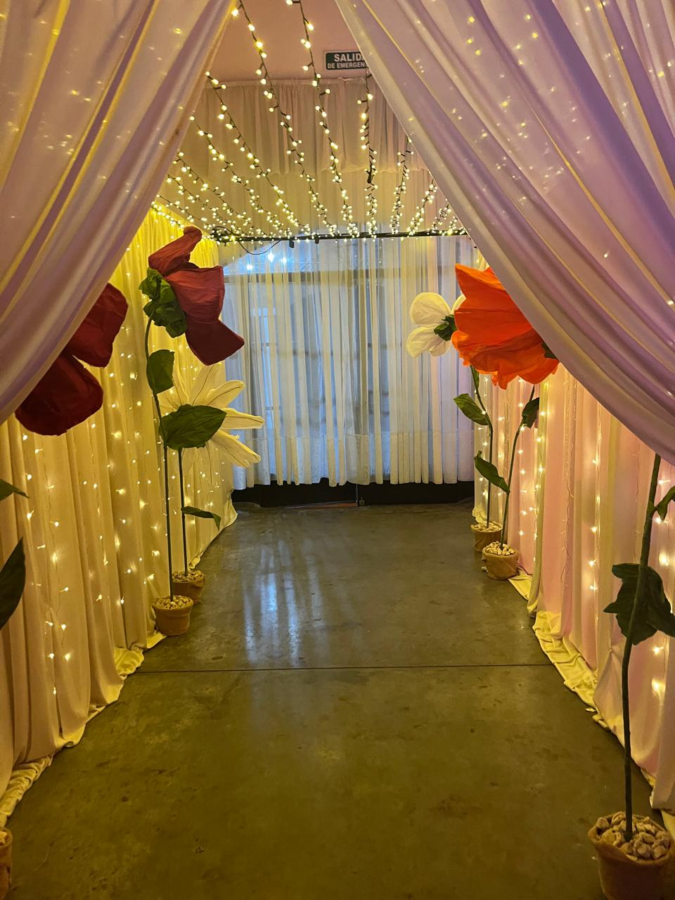 Un pasillo decorado con cortinas blancas ligeras, adornadas con grandes flores de papel en rojo, naranja y blanco.