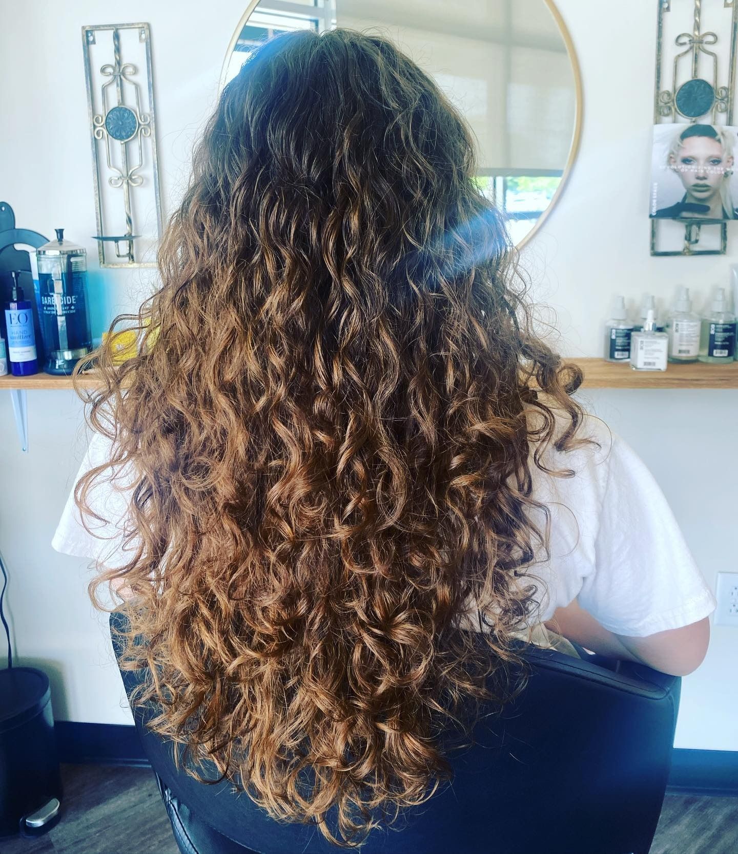 A woman with long curly hair is sitting in a chair in front of a mirror.