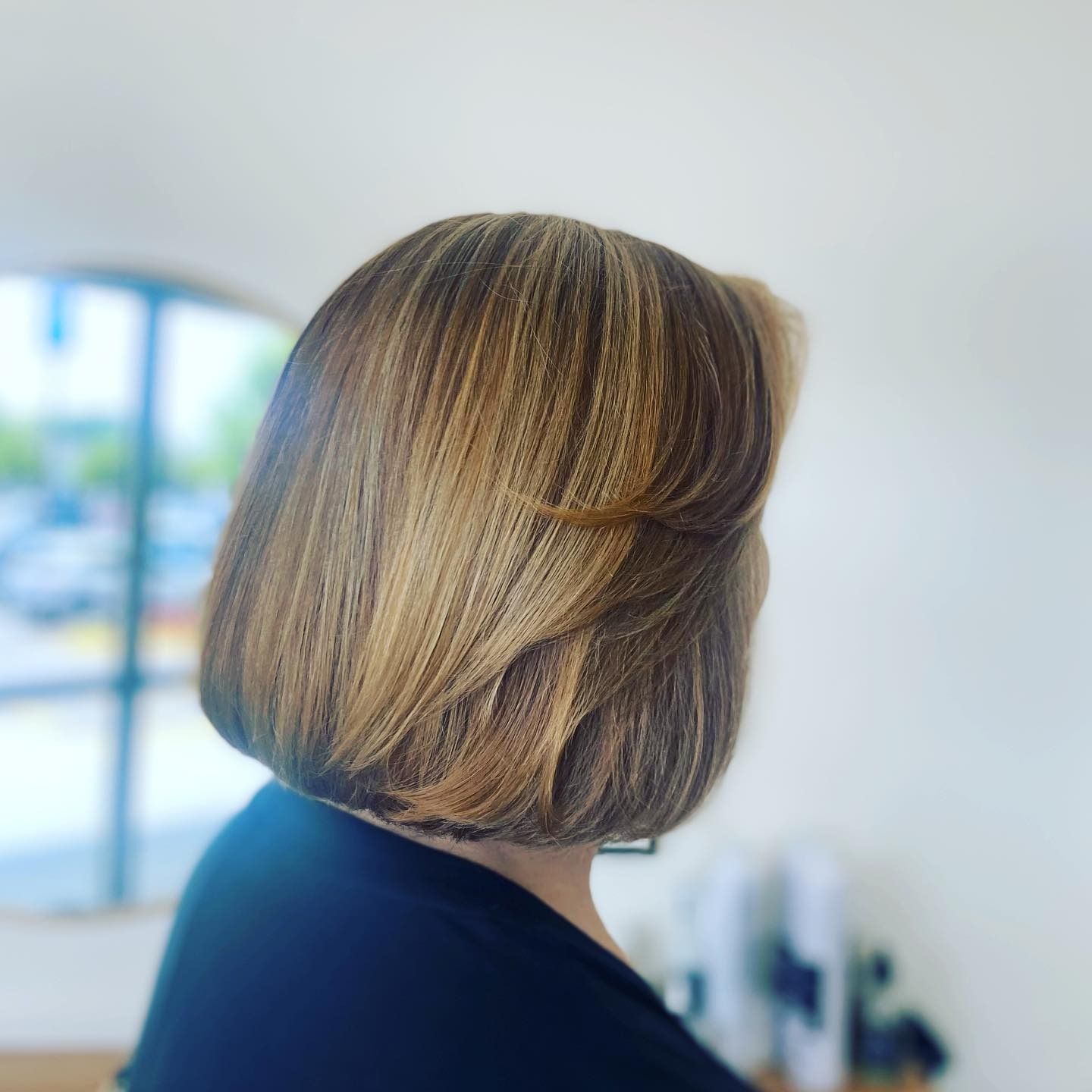 A woman with short brown hair is standing in front of a window.