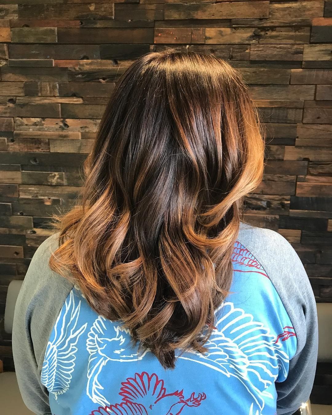 A woman with long brown hair is wearing a blue shirt with a bird on it.