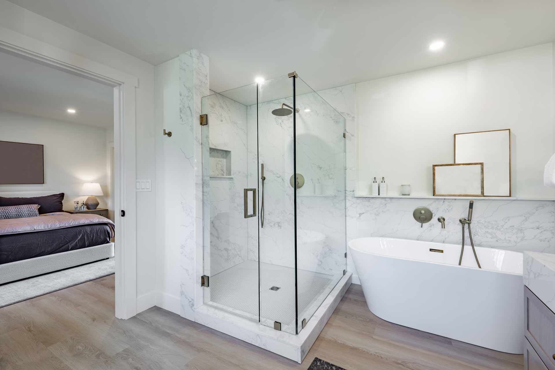 Modern bathroom with glass shower, bathtub, and view into bedroom; light-colored wood floor and white walls.