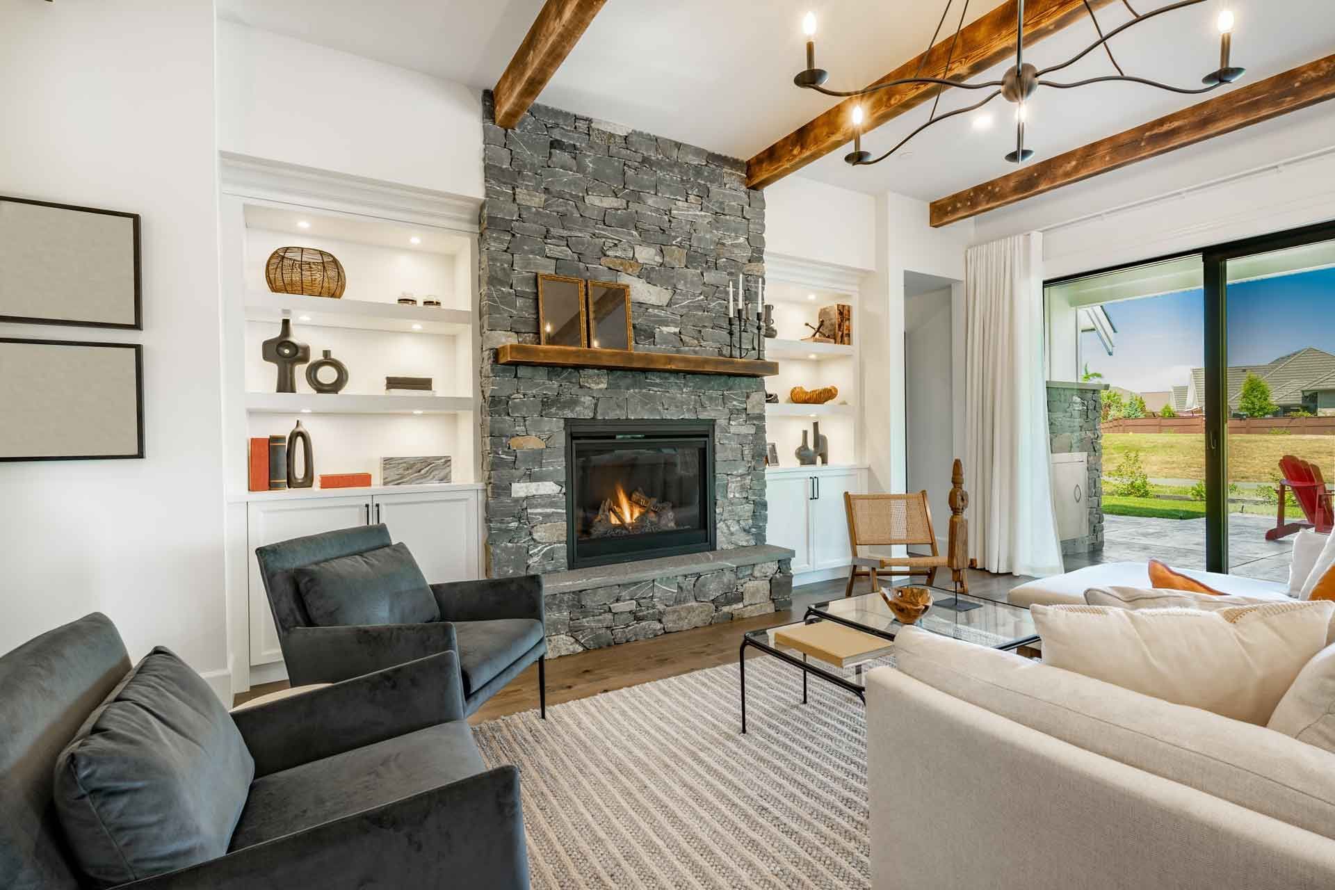 Cozy living room with stone fireplace, built-in shelves, grey chairs, and a sliding glass door to a patio.