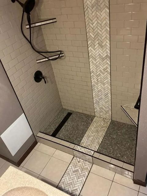 Shower with gray and white tile, pebble floor, and shelves.