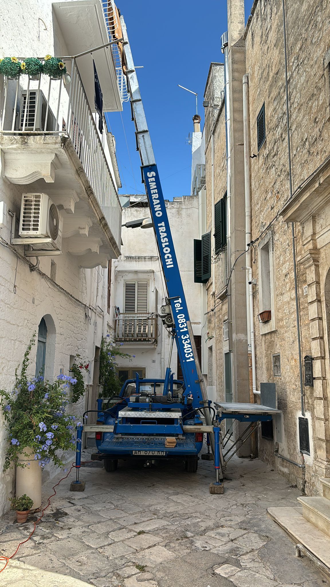Carrello elevatore blu in uno stretto vicolo tra edifici bianchi e in pietra.