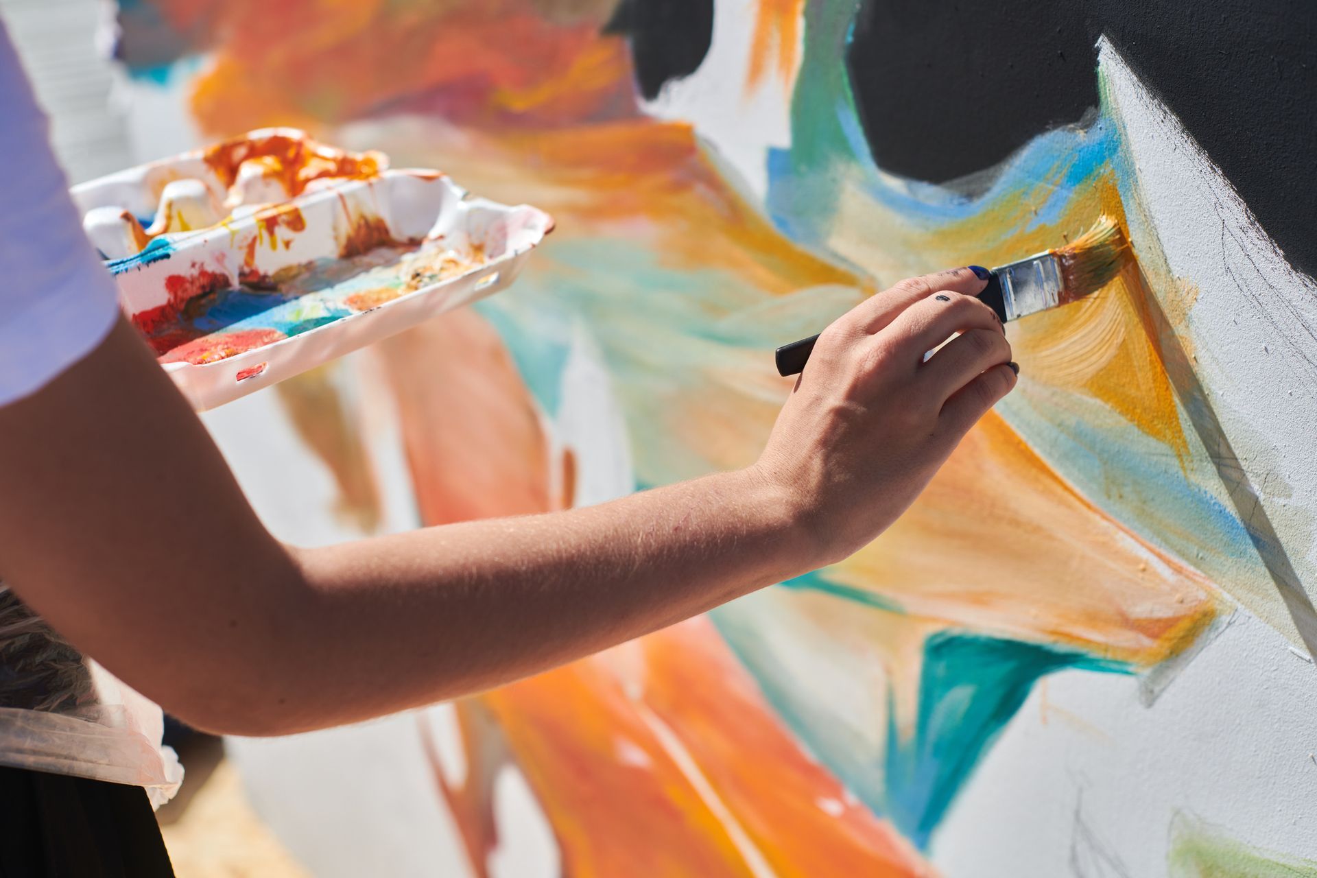 A person paints an abstract mural with a brush, holding a paint palette.