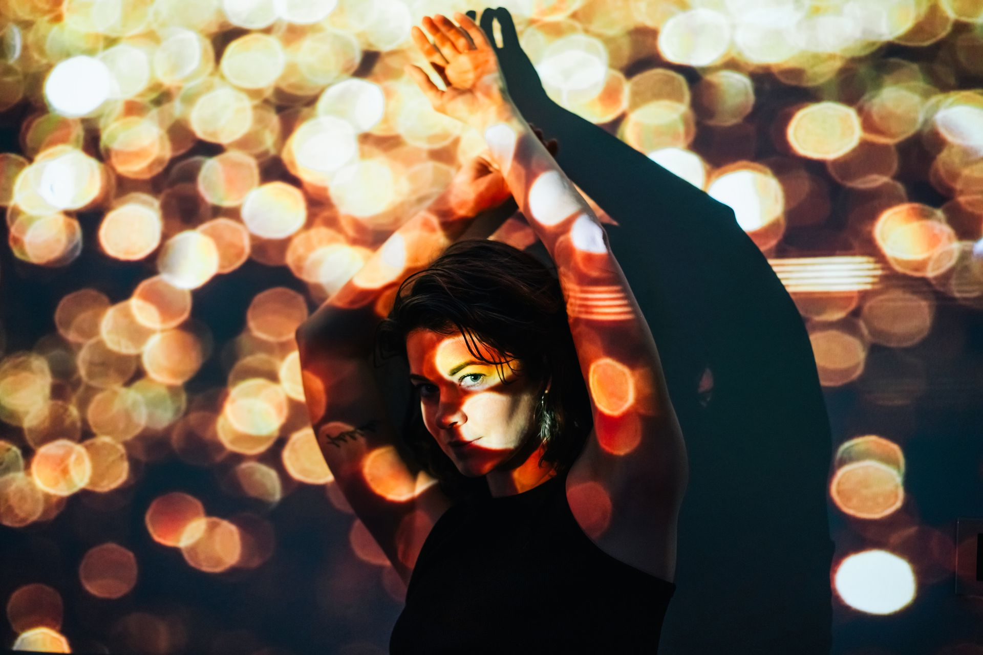 Woman with arms raised, illuminated by bokeh lights and shadow.