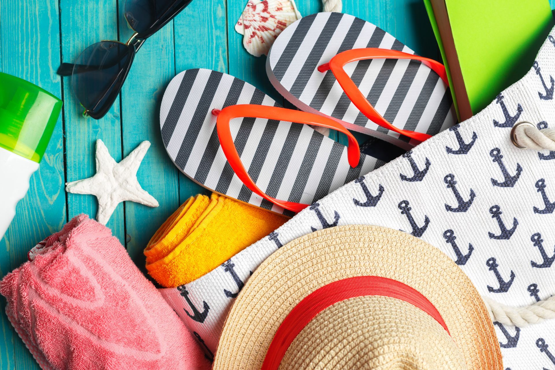 Beach essentials including flip flops, sunscreen, towel, and hat for vacation packing checklist