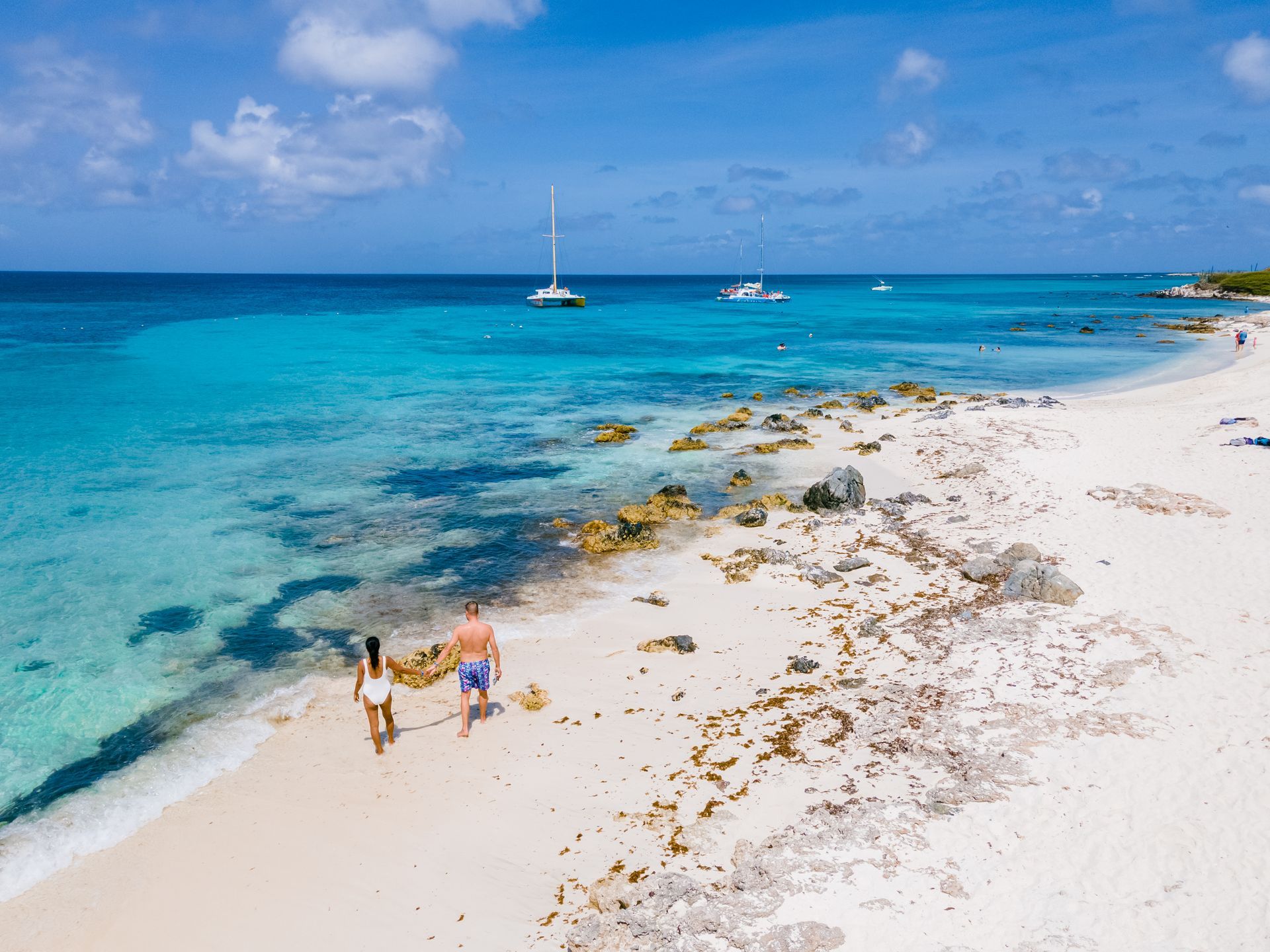 Couple walking along Eagle Beach in Aruba with clear turquoise water and tropical vacation scenery