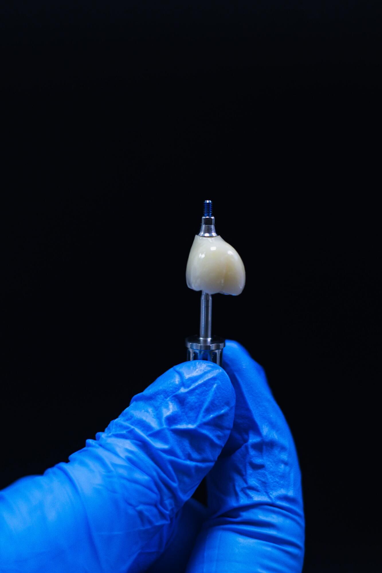 Gloved hand holding a small translucent sample on a tool against a black background