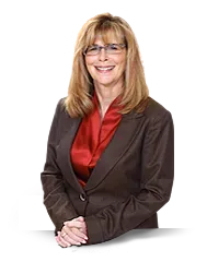 A woman wearing glasses and a brown jacket is standing with her hands folded.