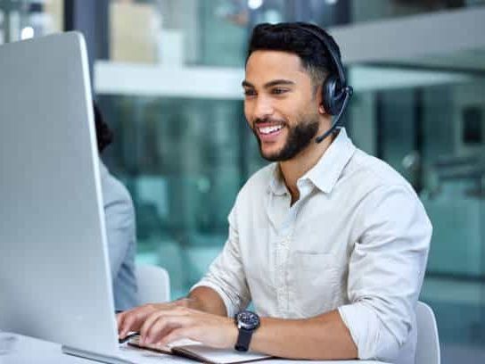 A man wearing a headset is sitting in front of a computer.