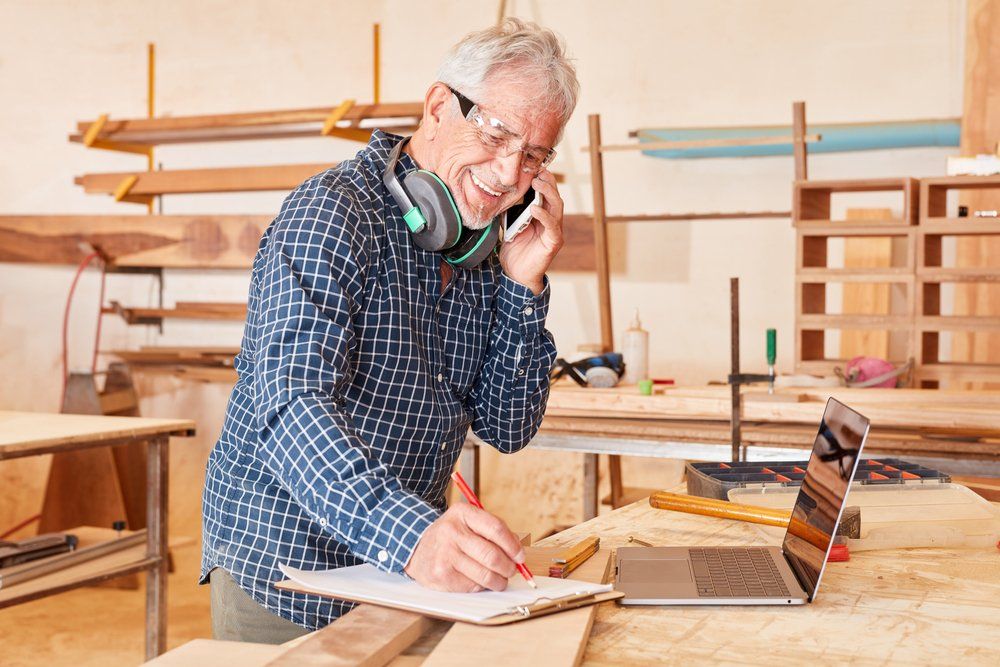 An older man is talking on a cell phone in a woodworking shop.