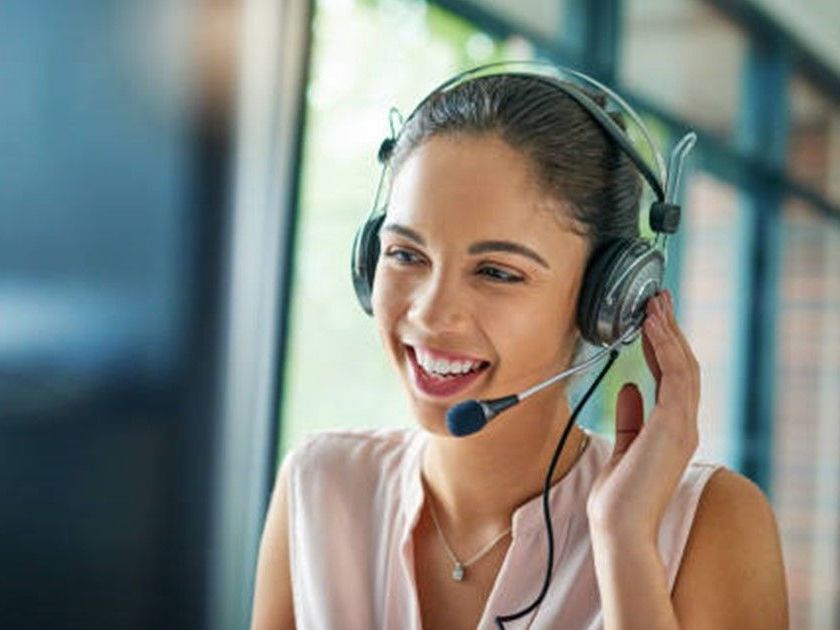 A woman wearing a headset is smiling while talking on a computer.