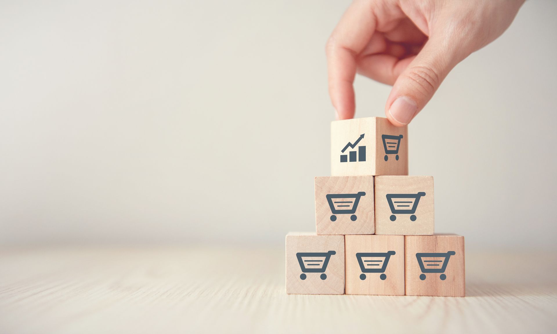 A person is stacking wooden blocks with shopping cart icons on them.