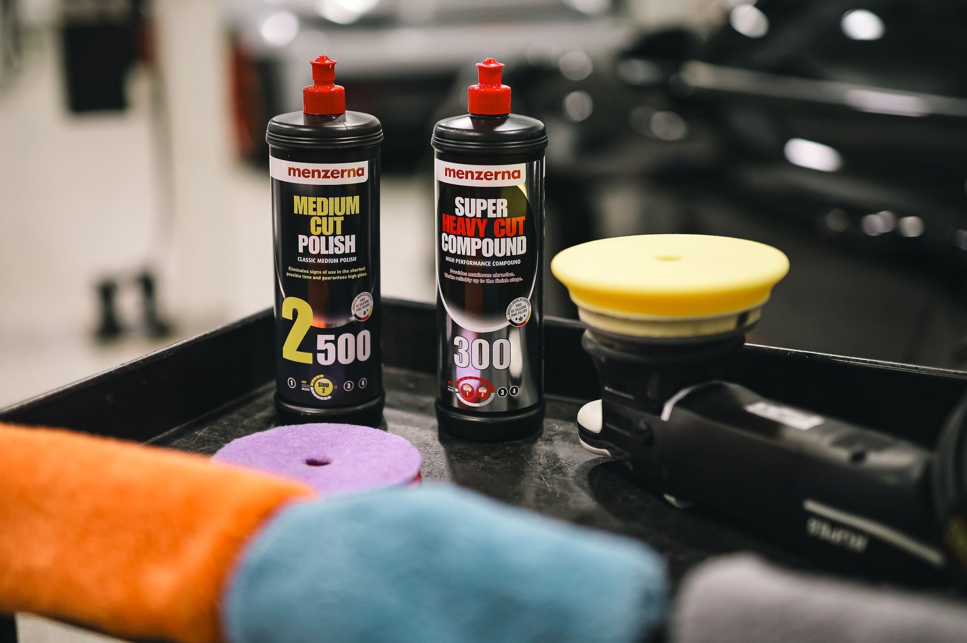 Two car detailing spray bottles beside microfiber towels and a yellow polishing pad on a black car surface