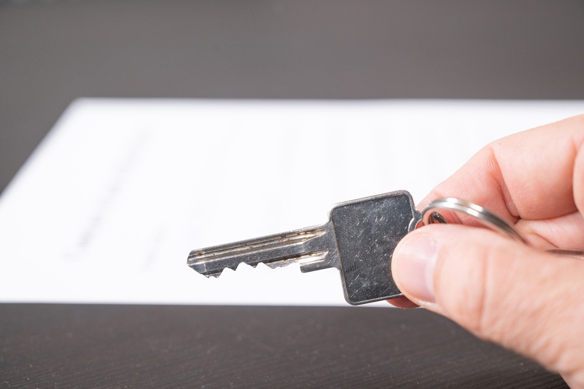 A hand holding a key next to a document, highlighting the importance of a title agency. A hand holding a key next to a document, highlighting the importance of a title agency.
