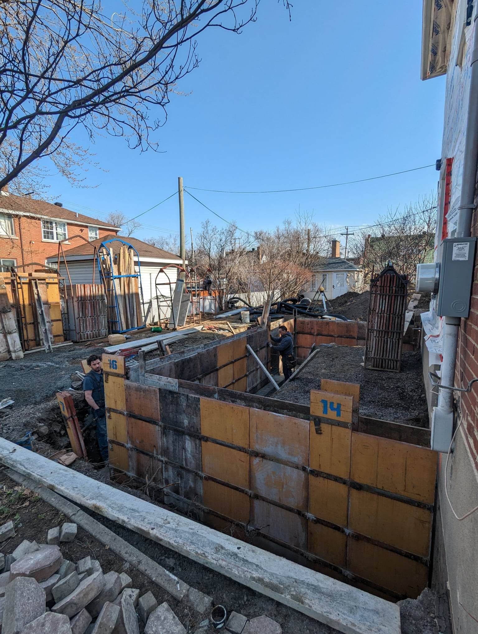 Chantier de construction avec des coffrages en béton orange, deux ouvriers et un ciel bleu dégagé.