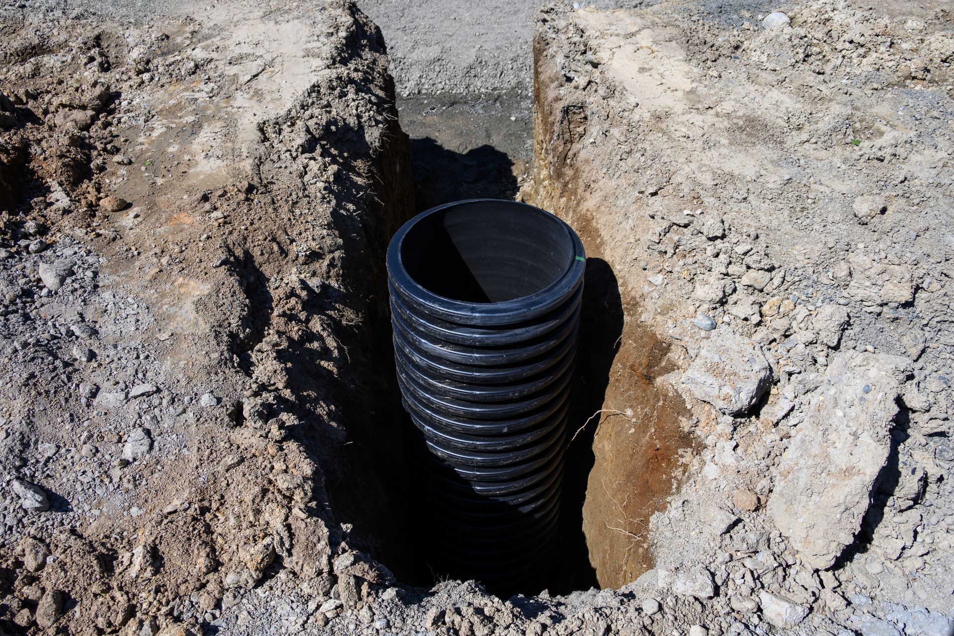Black corrugated pipe installed in a dirt excavation trench