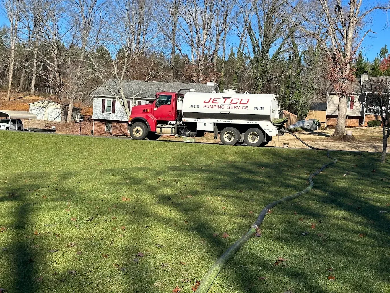 Red utility truck parked on a grassy yard near small houses and leafless trees on a sunny day