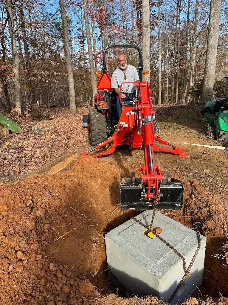 Orange excavator positioning a concrete block in a wooded trench site